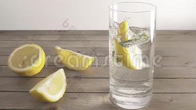 一片柠檬掉进透明的矿泉水和薄荷。 水溅在玻璃上。 慢动作。